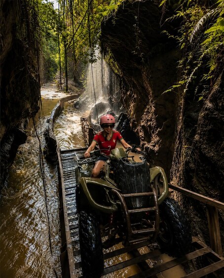 A person on a quad bike navigating a narrow water-filled path in a forested area. 4