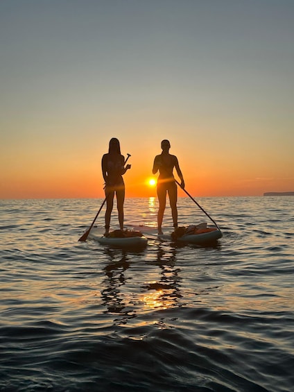 Two people paddleboarding on calm water during sunset. 2
