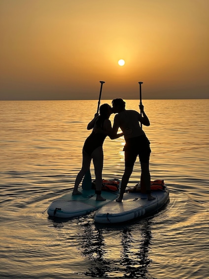 Two people on a paddleboard in calm waters at sunset. 1