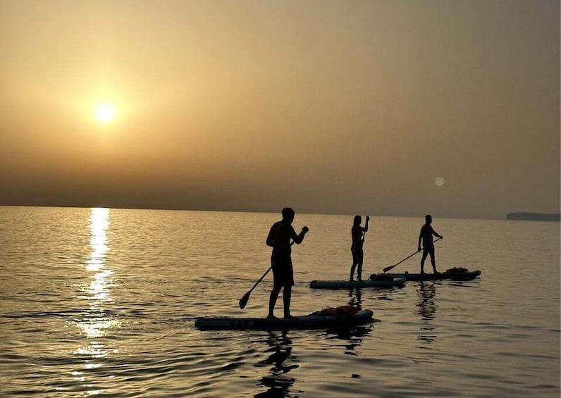 People paddleboarding on calm water during sunset. 3