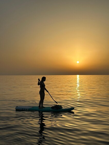 A person paddleboarding on calm water during sunset. 5