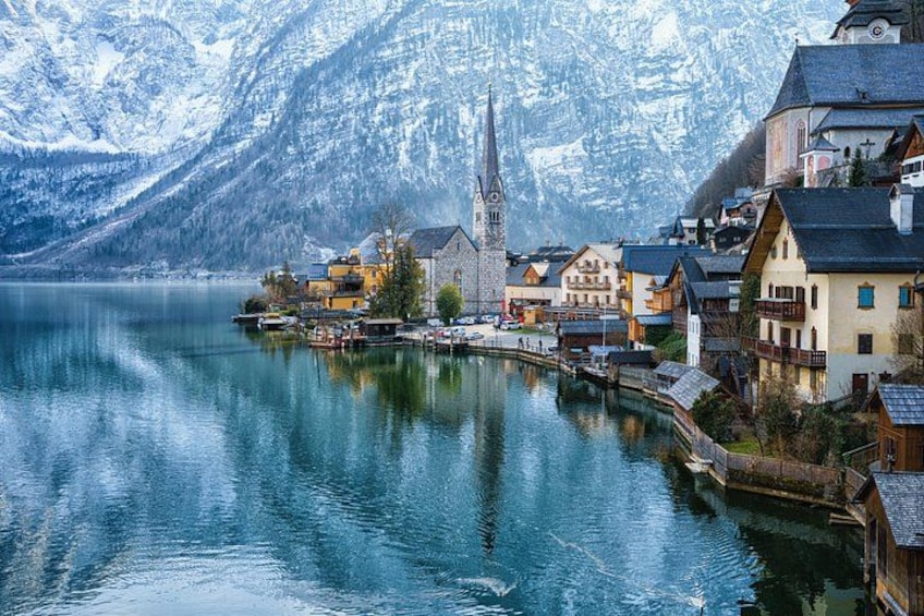 Une ville au bord d’un lac, avec des montagnes enneigées en arrière-plan, une église et des maisons aux couleurs vives qui bordent le rivage. 2