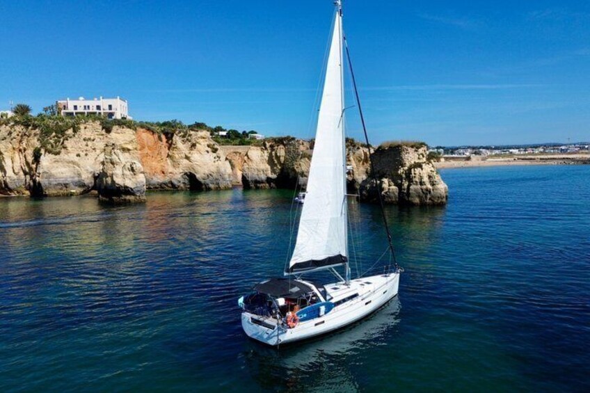 A sailboat on calm waters with a rocky coastline and a building in the background. 2