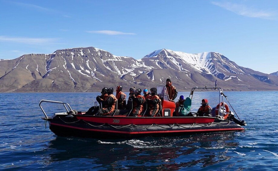 A group of people on a red boat with a number 760, sailing on a calm body of water with snow-capped mountains in the background. 2