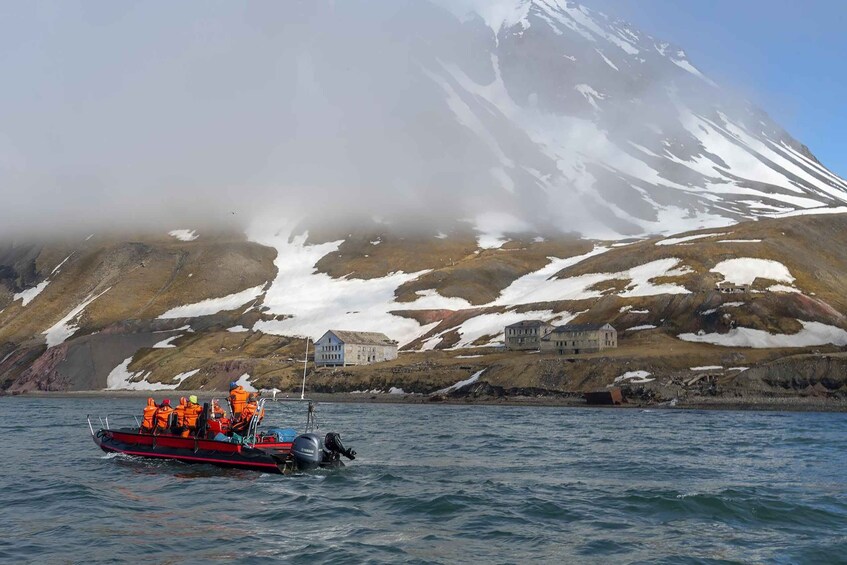 A boat with people wearing life jackets on a calm body of water, with snow-covered mountains in the background. 1