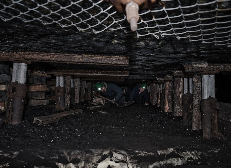 Miners working underground with headlamps, wooden supports, and mining tools. 5