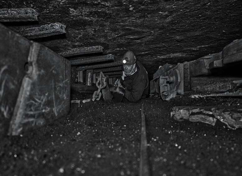 A person in a dark, confined space with wooden beams and machinery, wearing a helmet and safety gear. 3