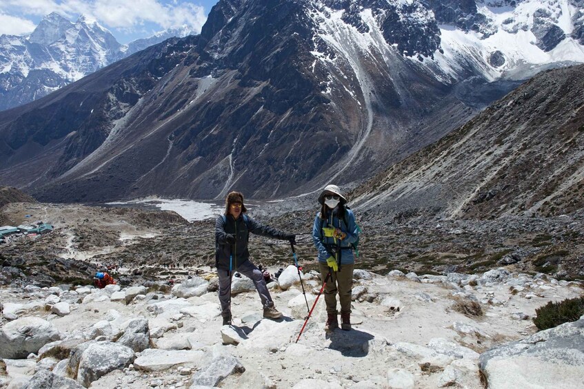 Two hikers on a rocky mountain trail with snow-capped peaks in the background. 4