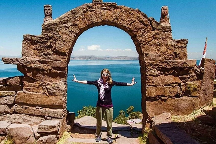A person standing in front of a stone archway with a view of a body of water and distant land. 2