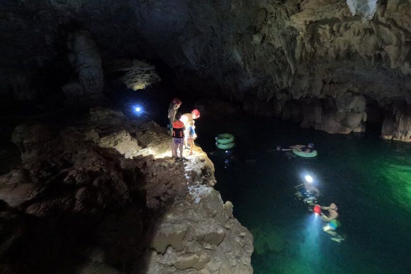 Una cueva con un cuerpo de agua, personas sobre un saliente y otras flotando. 3