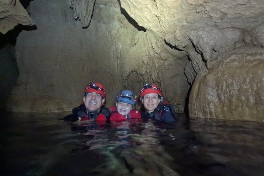 Three people in a cave with water, wearing helmets and life jackets. 4