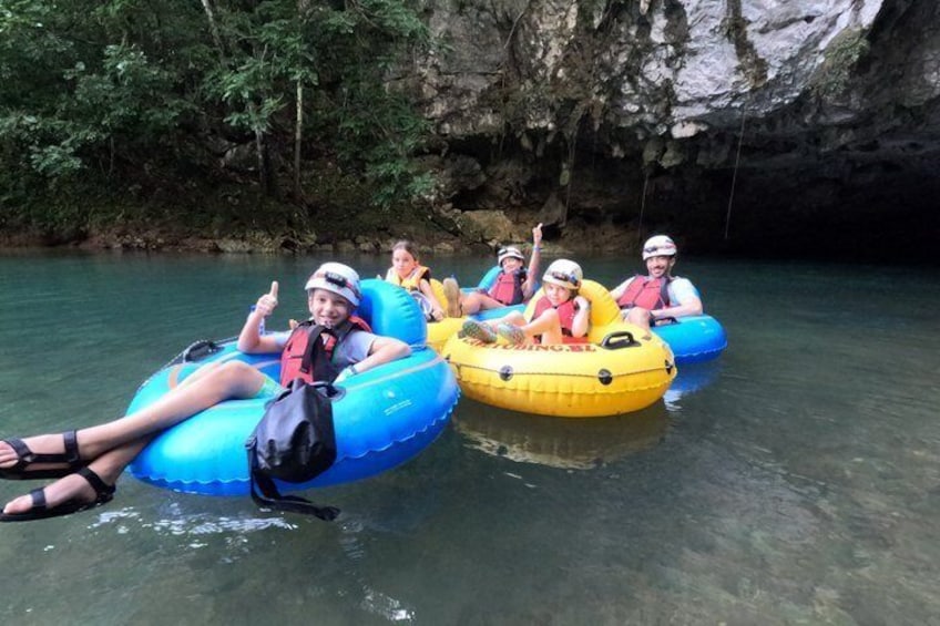 People on inflatable rafts in a river surrounded by greenery and rocky cliffs. 1