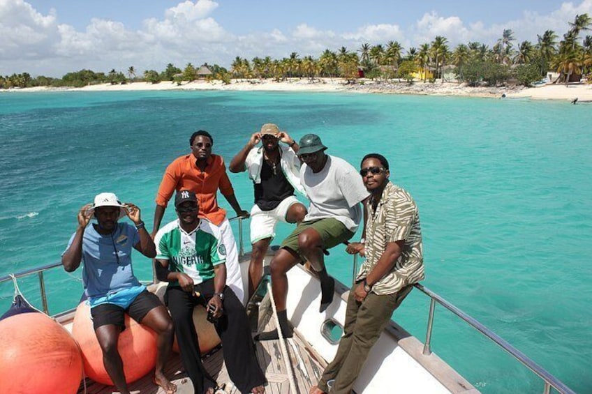 Un grupo de personas en un bote cerca de un mar turquesa, con una playa y palmeras al fondo. 2