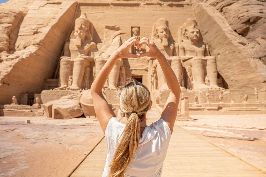 A person making a heart shape with their hands in front of a large ancient Egyptian temple. 1