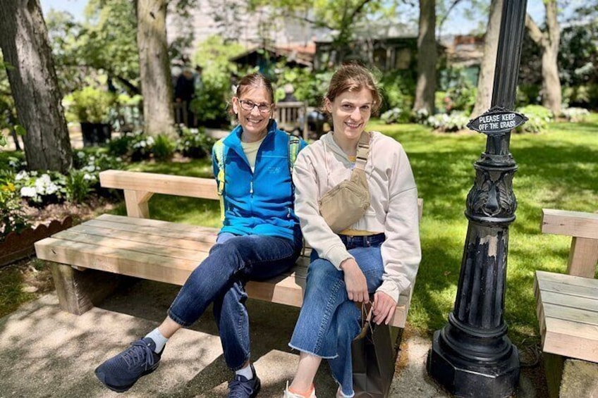 Two people sitting on a bench in a park with a sign that says 'PLEASE KEEP OFF THE GRASS.' 3