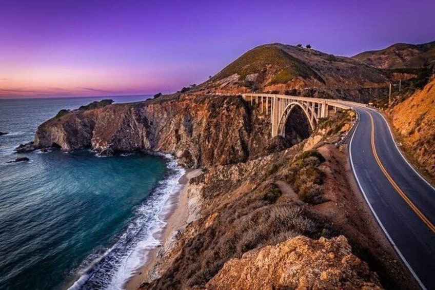 Une route côtière avec un pont enjambant l’océan, des falaises rocheuses et un ciel au coucher du soleil. 2