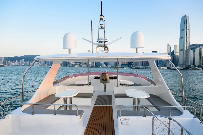 A yacht with a white deck, seating, and a city skyline in the background. 1