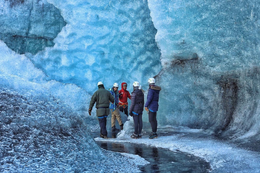 A group of people standing on a frozen surface near a large ice formation. 3