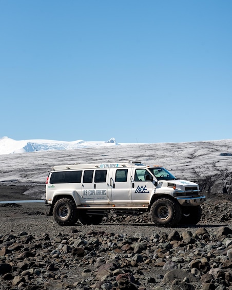 A white SUV with 'ICE EXPLORERS' branding parked on a rocky terrain with a glacier in the background. 4