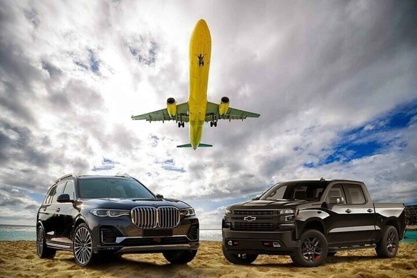 A black SUV and a pickup truck on a beach with a plane flying overhead. 1