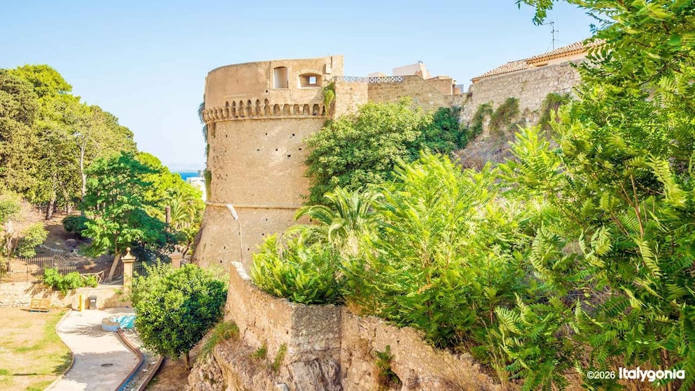 A historic stone fortress with a round tower, lush greenery, and a clear sky. 2
