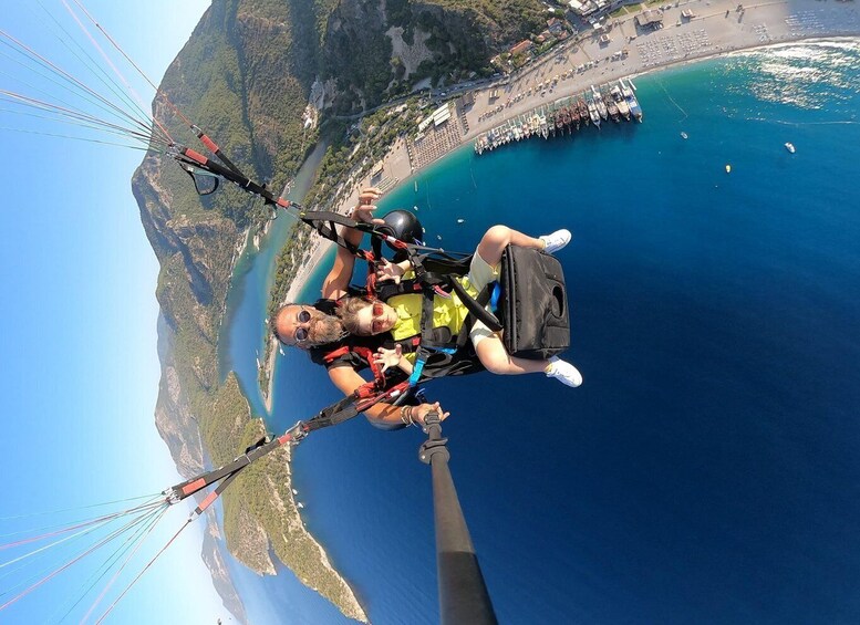 A person paragliding over a coastal area with a clear view of the sea, boats, and a beach. 5