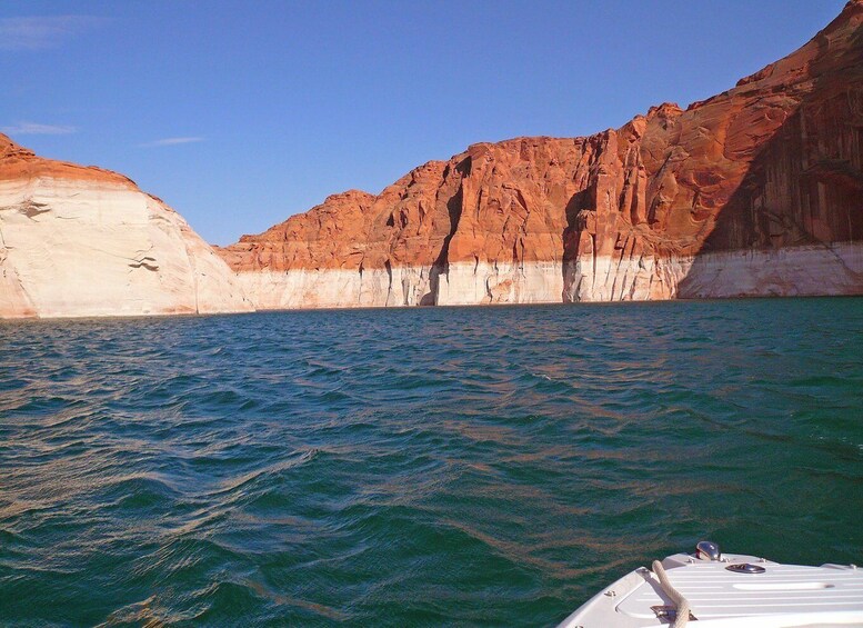A boat on a body of water with red and white rock formations in the background. 2