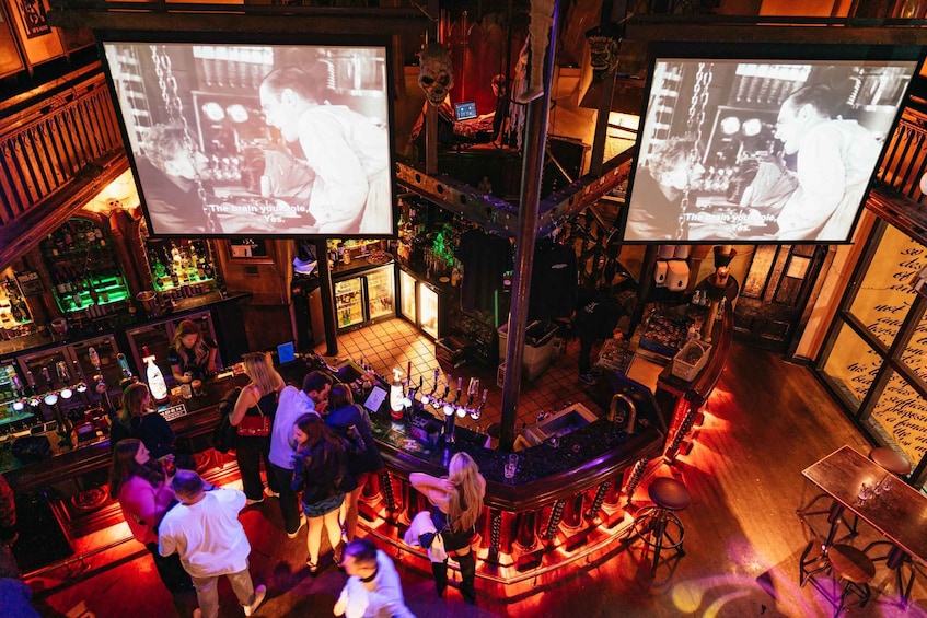 A bar with multiple screens displaying content, a crowd of people, and a variety of bottles and glasses on shelves. 2