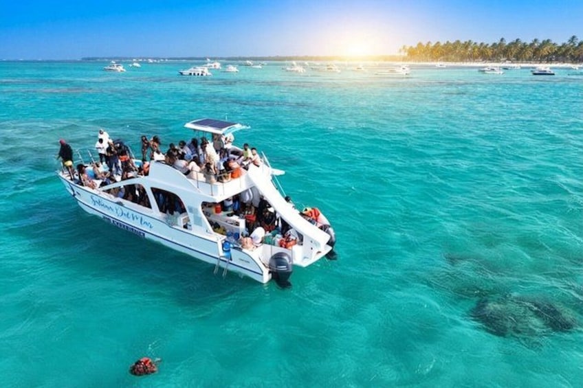 A boat with passengers on a turquoise sea, surrounded by other boats and a beach with palm trees. 1