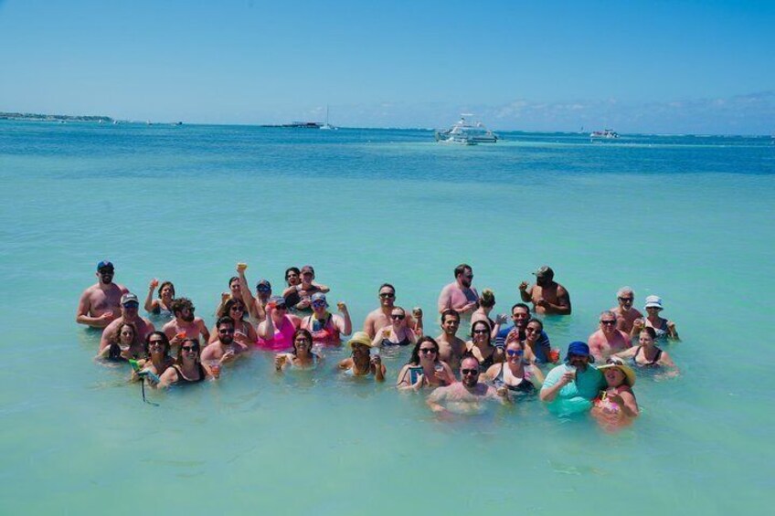 Un grupo de personas nadando en agua azul cristalina, con barcos al fondo. 4