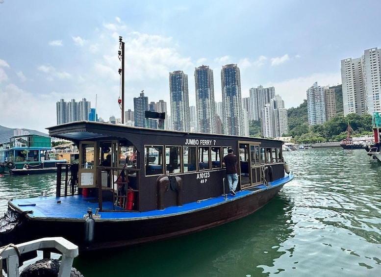 A ferry named 'Jumbo Ferry 7' with passengers, docked at a harbor with high-rise buildings in the background. 1