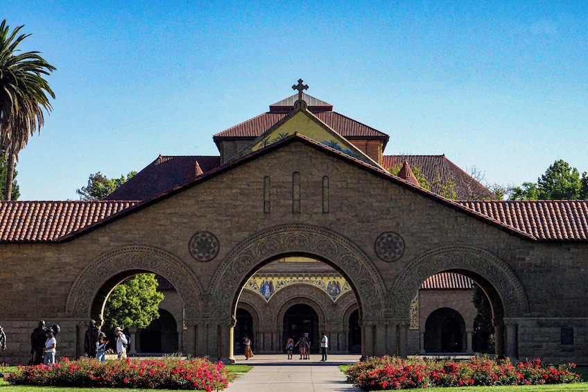 A historic building with a tiled roof, an ornate archway, and a cross on top. 2