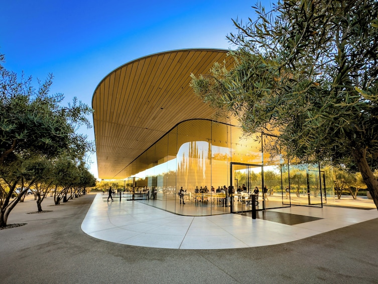 A modern architectural building with a curved roof and glass facade, surrounded by trees and a paved plaza. 5