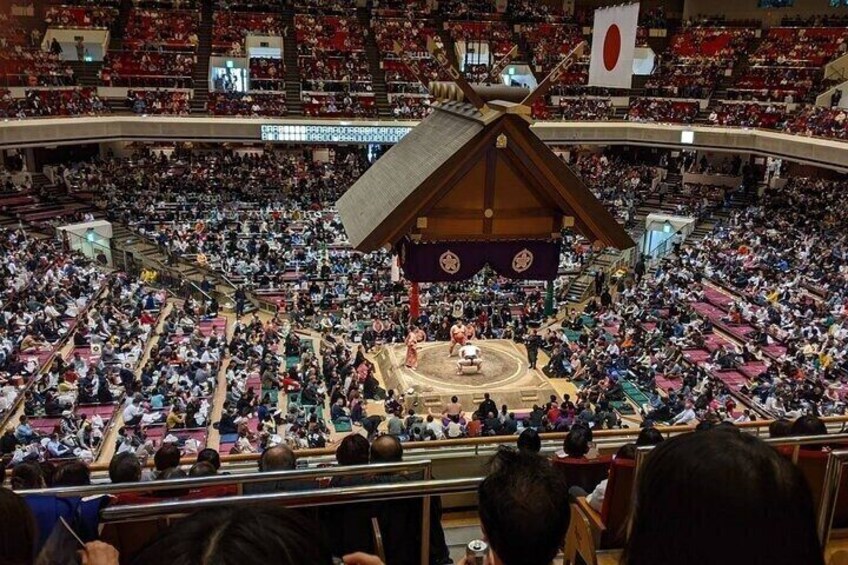 Un gran espacio interior tipo arena, con un ring central rodeado de espectadores. 1