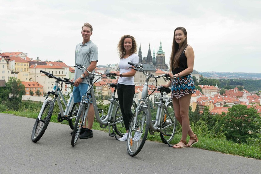 Three people standing on a path with bicycles, overlooking a cityscape with historic buildings and a clock tower. 5