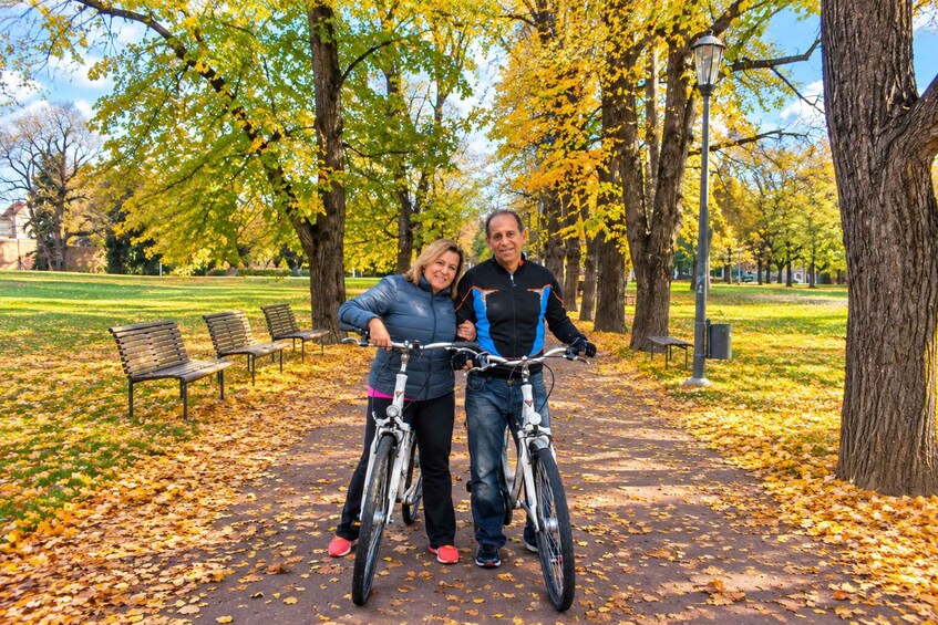 A couple on bicycles in a park with autumn leaves on the ground. 3