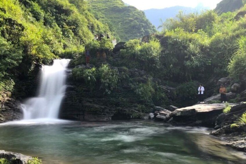A waterfall in a lush green valley with rocky terrain and a person standing on a rock. 2