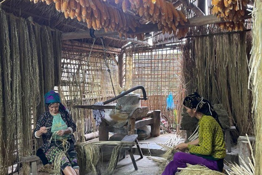 Two women seated in a rustic, thatched-roof structure with woven baskets and corn cobs. 5