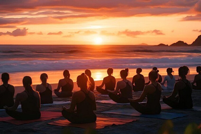 Un grupo de personas meditando en una playa al atardecer. 2