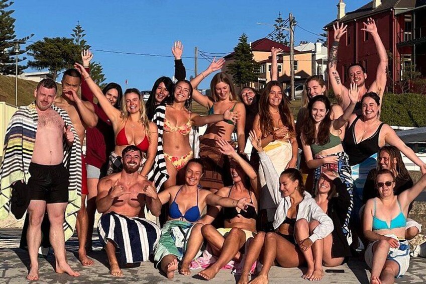 Un grupo de personas posando al aire libre, algunas con traje de baño, con edificios y árboles de fondo. 3