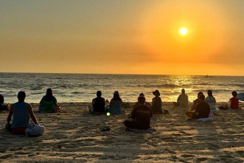 A group of people sitting on a beach at sunset. 1