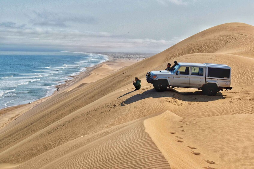 A white off-road vehicle parked on a sand dune with footprints leading up to it, overlooking a beach and ocean. 5