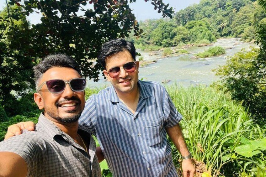 Two people standing by a river with greenery in the background. 3