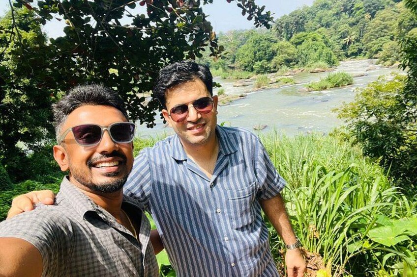 Dos personas de pie junto a un río, con follaje en el fondo. 2