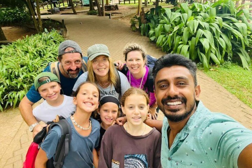A group of people taking a selfie in a park with a paved walkway and green foliage. 4