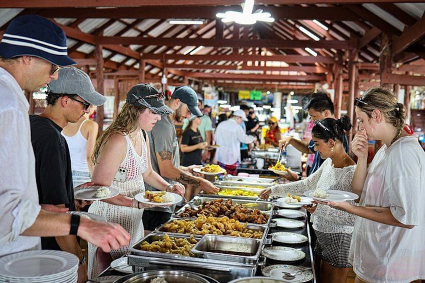 A food stall with various dishes and people serving and eating. 2