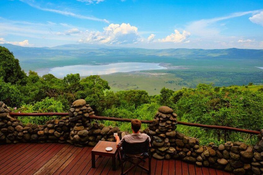 A person sitting at a table on a wooden deck overlooking a valley with a lake and mountains. 5