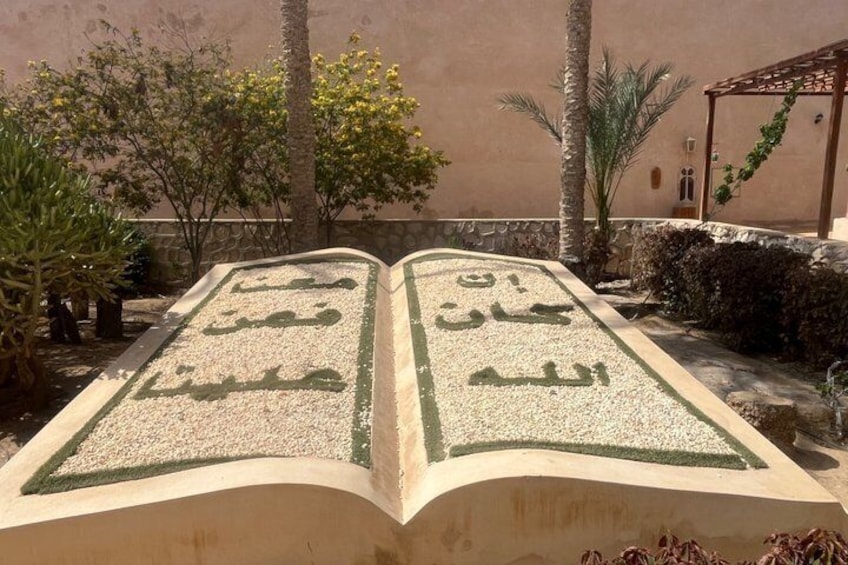 Un libro abierto con caligrafía árabe sobre un sendero de jardín. 1