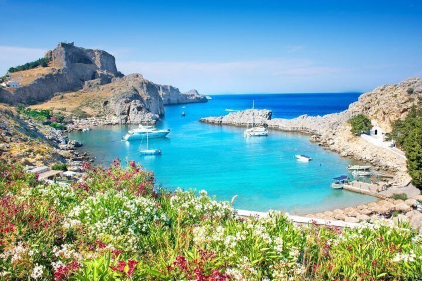 A coastal landscape with boats, rocky cliffs, and a clear blue sea. 3