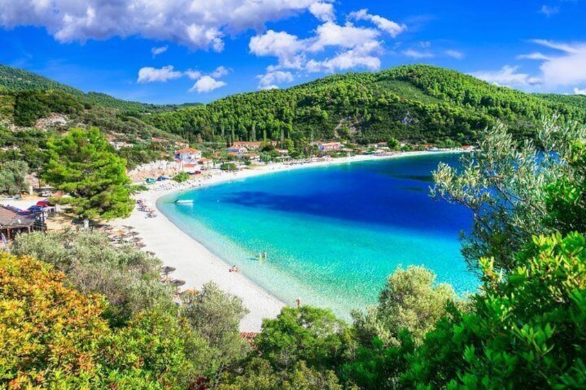 A coastal landscape with a beach, clear blue waters, and green hills. 5